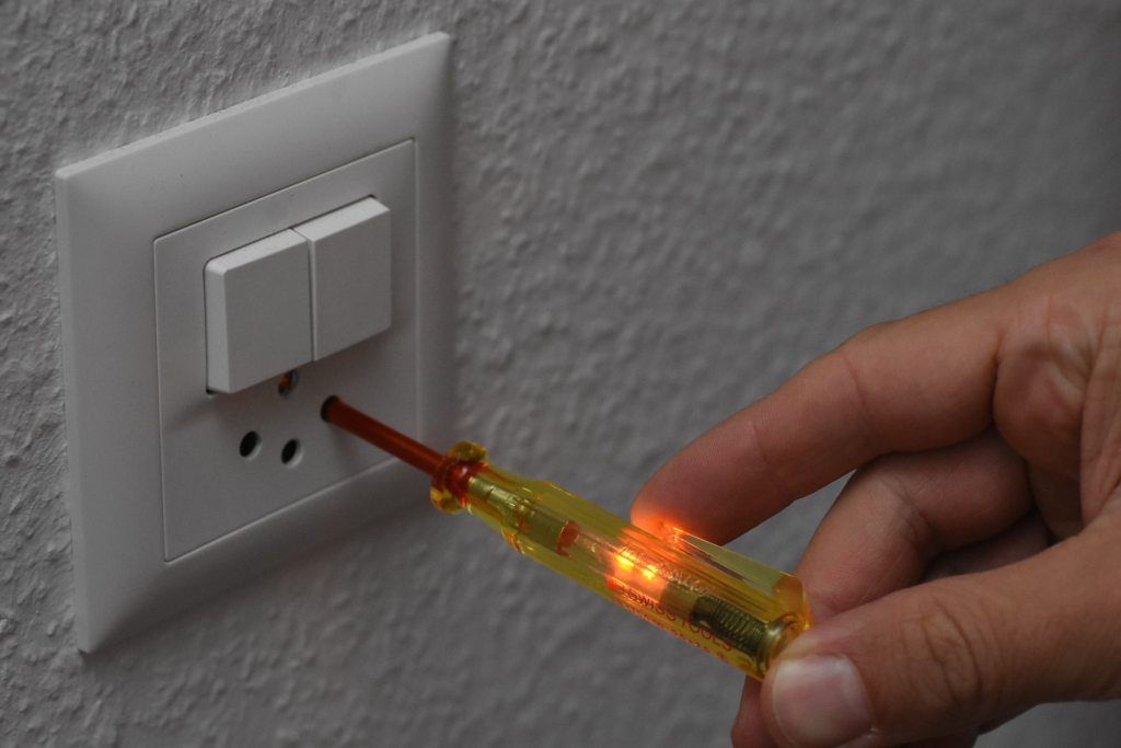 A yellow screwdriver-style test light being inserted into a power socket. The test light inside the screw driver is lit up.